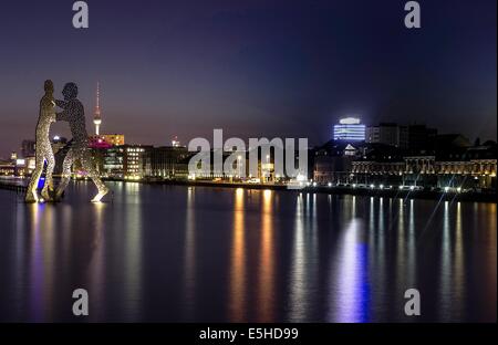 Berlin, Deutschland. 31. Juli 2014. Die Lichter der Stadt spiegeln sich in der Spree in Berlin, Deutschland, 31. Juli 2014. Der neue "Osthafen" Industriepark gilt gegenüber dem Kunstwerk "Melcule Men" (L) des US-Künstlers Jonathan Borofsky. Foto: PAUL ZINKEN/Dpa/Alamy Live News Stockfoto