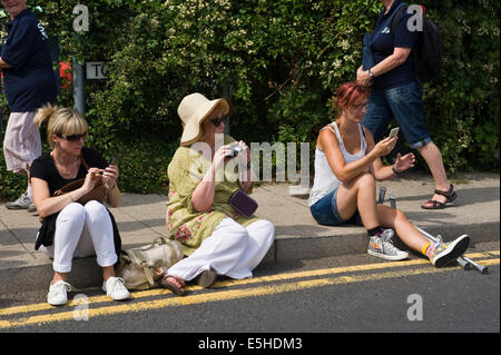 Drei Frauen saßen auf Bordstein mit Smartphones und digitalen Kameras zu fotografieren Oyster Festival in Whitstable Kent England UK Stockfoto