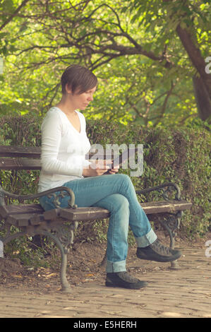 Frau mit digitalen Tablet-Computer und Surfen im Internet auf einer Holzbank im Park sitzend. Stockfoto