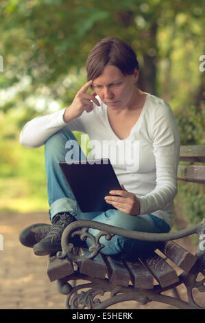 Frau mit digitalen Tablet-Computer und Surfen im Internet auf einer Holzbank im Park sitzend. Stockfoto