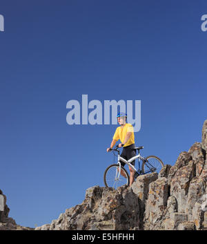 Mountainbiker steht auf einer felsigen Klippe mit seinem Motorrad Stockfoto