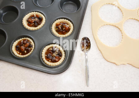 Mince Pies machen in der Küche - gefüllte Gebäck Fällen, Hackfleisch, Teig Fetzen und Teelöffel Stockfoto