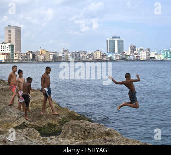 Jugendlichen Tauchgänge ins Meer vor der Küste von Havanna, Malecon mit der Skyline von Gebäuden im Hintergrund Stockfoto