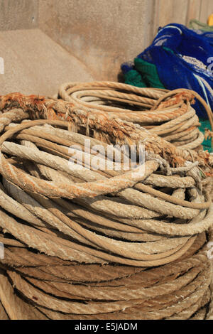 Spulen aus verwitterten Seil am Kai in der Fischerei Hafen von Llanca, Catalonien, mit Netzen im Hintergrund. Stockfoto