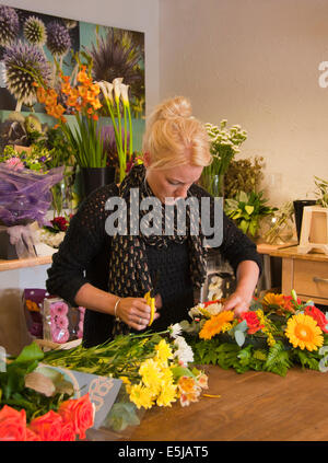 Floristen arrangieren einen Kranz in einem Blumenladen mit Trauben von Blumen und eine Blume Poster im Hintergrund. Stockfoto