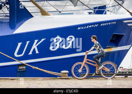 Niederlande, Urk, Frau mit Ast Fahrrad vor Fischereifahrzeug. Das Dutch Design aus Holz-Bike ist eine Schöpfung von Jan Gunneweg Stockfoto