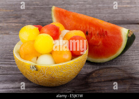 Melonenkugeln in Schüssel geben, eine Melone auf hölzernen Hintergrund gemacht Stockfoto