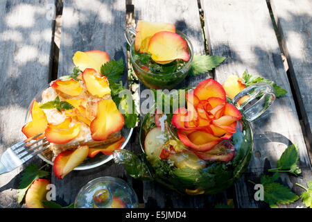 Rose und Minze Tee in transparenten Teekanne und Teetasse und Kuchen dekoriert mit Rosenblättern auf Holztisch Natur Stockfoto
