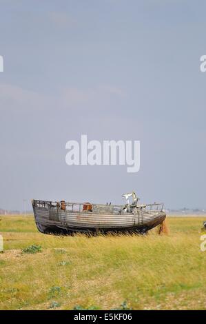 Verlassene verlassene Fischerboot, das auf dem grasbedeckten Kiesstrand über dem hohen Wasser aufgestellt wurde. Dungeness, Kent, England, Großbritannien. Stockfoto