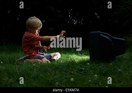 Kind blonde junge Fernsehen in Hof, draußen im grünen Rasen, emotionale, Gesichts Ausdruck, Grimassen schneiden, Grinsen Stockfoto