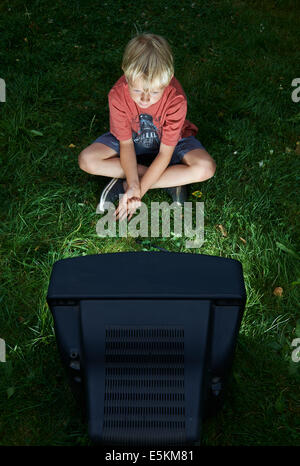 Kind blonde junge Fernsehen in Hof, draußen im grünen Rasen, emotionale, Gesichts Ausdruck, Grimassen schneiden, Grinsen Stockfoto