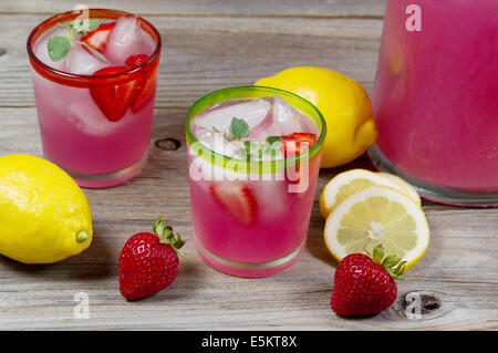 Top Vorderansicht eines Glases gefüllt mit frisch zubereiteten rosa Limonade mit ganzen Zitronen, Erdbeeren und eine partielle Krug Stockfoto