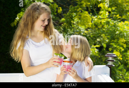 Seitenansicht der Schwestern umarmen einander beim trinken kalte Limonade im Freien auf der Terrasse Stockfoto