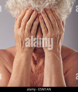 Close-up Portrait einer traurig aussehende senior Frau mit dem Kopf in die Hände vor grauem Hintergrund. Verärgert über ihr alte Stockfoto