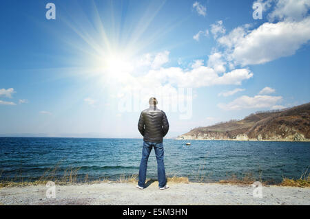 Mann in einem schwarzen Jacke steht am sonnigen Himmel Meer Hintergrund Stockfoto