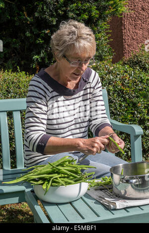 Ältere Frau mit rheumatoider Arthritis im Garten Königreich schneiden selbst angebautes grün/Stangenbohnen bereit zur späteren Verwendung einfrieren Stockfoto