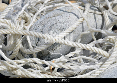 Alten Seil gewaschen auf der Küste und zwischen abgerundete Felsen verstrickt. Stockfoto