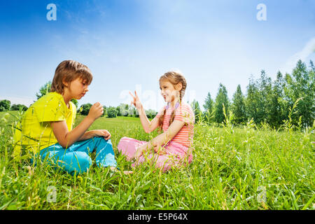 Mädchen und Jungen spielen Rock-Paper-Scissors auf Rasen Stockfoto