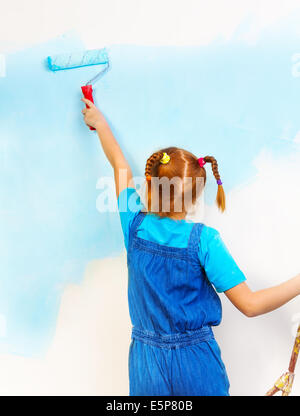 Kleines Mädchen im blauen Lätzchen und Klammer malt die Wand Stockfoto