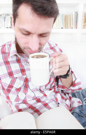 legerer Mann trinken Kaffee oder Tee und Lesebuch entspannen zu Hause Stockfoto