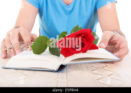 junger Mann mit seinen Händen halten aufgeschlagene Buch während rote rose und die Gläser sind drauf Stockfoto