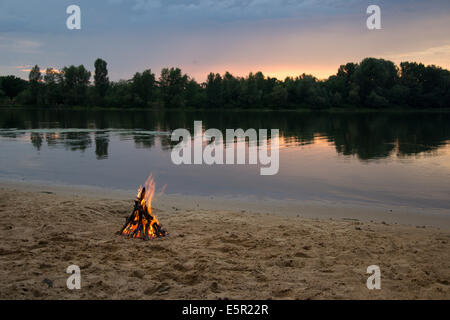 Lagerfeuer am Ufer des Flusses bei Sonnenuntergang Stockfoto