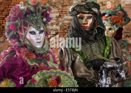 Mann in aufwendigen braun Kostüm mit Schlange von zwei Frauen in ausgefallenen Kostümen während des Karnevals in Venedig flankiert. Stockfoto