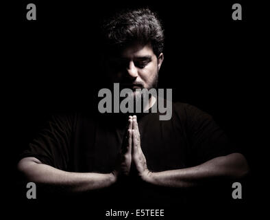 Lizenz erhältlich unter MaximImages.com - dramatisches Porträt eines Mannes aus dem Nahen Osten mit gefalteten Händen in einem Gebet oder Meditation isoliert auf Schwarz Stockfoto