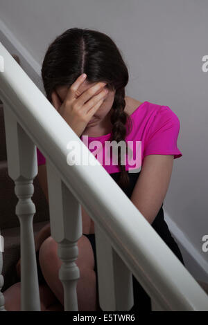 Junge weibliche Hände trägt ein pinkes Top und Haar in Plats sitzt auf der Treppe im Innenbereich auf Gesicht. Stockfoto