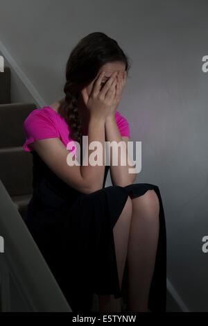 Junge weibliche Hände trägt ein pinkes Top und Haar in Plats sitzt auf der Treppe im Innenbereich auf Gesicht. Stockfoto