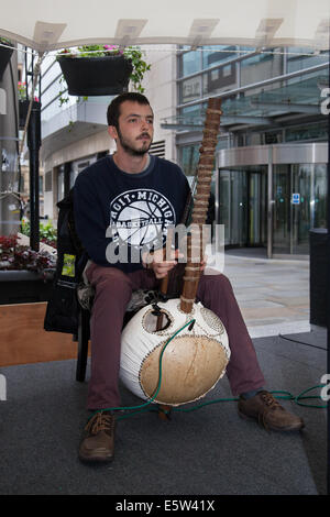 Der Busker John Haycock spielte das Kora String Instrument während des Urban Gardening Festivals Dig the City Deansgate, Manchester, das vom Business Improvement District in Manchester durchgeführt wurde – BID. Blumenschmuck, Bushaltestellen und ein Vimto-Garten verwandeln das Stadtzentrum von Manchester, als Dig the City zurückkehrte. Sechzehn Schaugärten, die während des Urban Gardening Festivals vom 2. Bis 10. August zu sehen sind. Jedes wurde speziell für die Veranstaltung entworfen, wobei ihre Designer die Herausforderungen des Gartenbaus in einem kleinen städtischen Raum annehmen müssen. Stockfoto