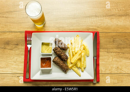 Traditionellen rumänischen Mici und Pommes Frites mit Ketchup, Senf und Bierglas Stockfoto