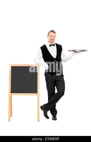 In voller Länge Portrait von männlichen Kellner halten einen leeren Schacht und stützte sich auf einer Tafel Stockfoto