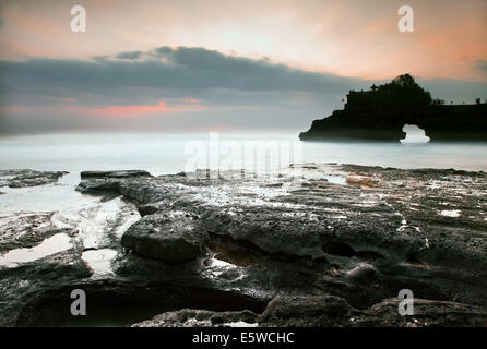 Lange Belichtung Bild des Sonnenuntergangs an einem natürlichen Felsbogen Küsten Funktion gegen Misty und geisterhaften Meerwasser bei Tanah Lot Tempel auf Bali Silhouette Stockfoto