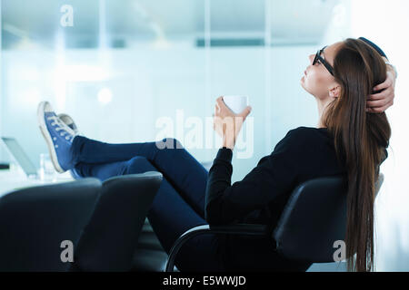 Weibliche Büroangestellte mit Füßen zurück stützte sich auf Konferenztisch Stockfoto