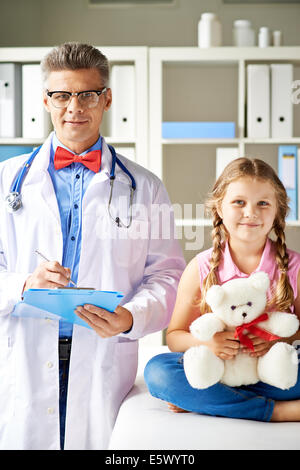 Fröhliche Mädchen mit Teddybär und ihr Blick in die Kamera im Krankenhaus Arzt Stockfoto