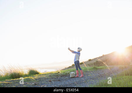 Junge Frau nehmen Foto auf Hügel bei Sonnenuntergang Stockfoto