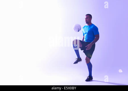 Studioaufnahme des jungen männlichen Fußballer Ball Mitte Luft mit Knie halten Stockfoto