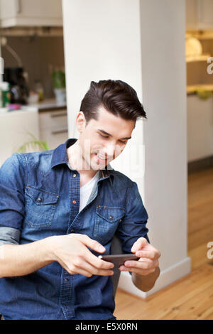 Junger Mann, Blick auf Smartphone in Küche Stockfoto