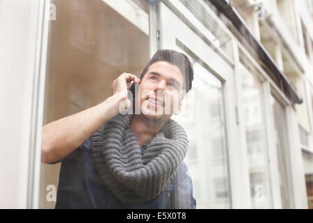 Junger Mann im Chat auf Smartphone hinter Terrasse Glas Stockfoto