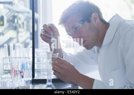 Junge männliche Wissenschaftler Pipettieren in Becherglas im Labor Stockfoto