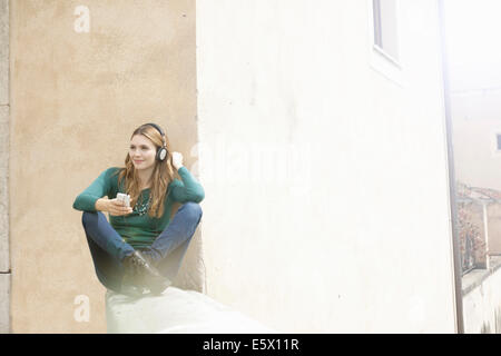 Junge Frau sitzt cross legged anhören von Musik über Kopfhörer Stockfoto