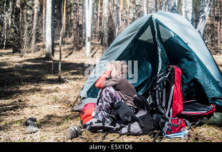 Junge mit Händen übers Gesicht sitzen außerhalb Zelt im Wald Stockfoto