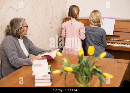Zwei Schwestern, die Klavier spielen beobachtet von Großmutter Stockfoto