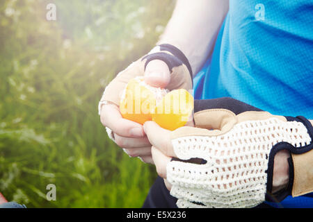 Radfahrer peeling Orange mit behandschuhten Händen Stockfoto