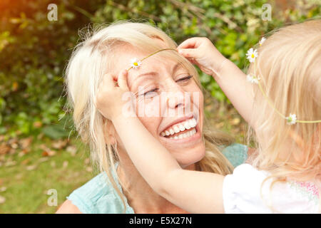 Nahaufnahme eines weiblichen Kleinkind Daisy-Chain in Mutters Haare im Garten platzieren