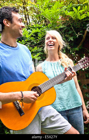 Junger Mann spielt akustische Gitarre im Garten für Freundin Stockfoto