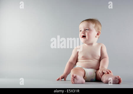 Studioportrait von Babymädchen sitzen und wegsehen Stockfoto