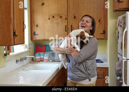 Mitte Erwachsene Frau tragen und streicheln Hund in Küche Stockfoto