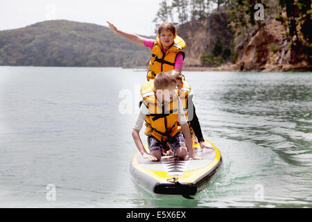 Brüder und Schwester, stehend und kniend auf Paddleboard auf hoher See Stockfoto